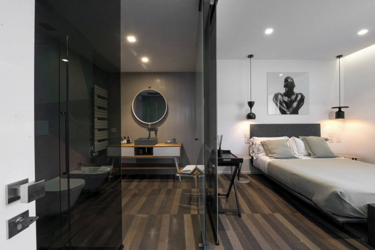 Un dormitorio moderno con cama, mesita de noche, lámpara y espejo en la pared.