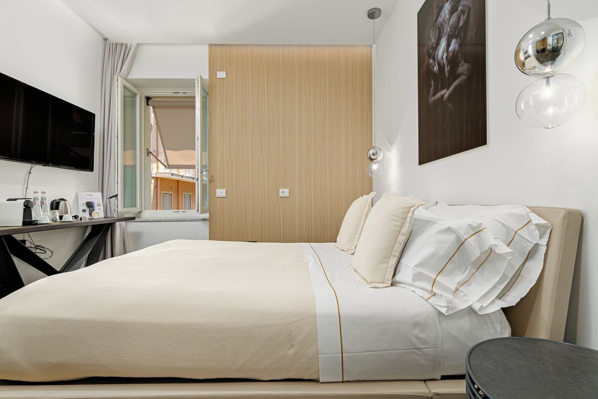A hotel room with a bed, a TV, a desk with a lamp, and a view of the outside.