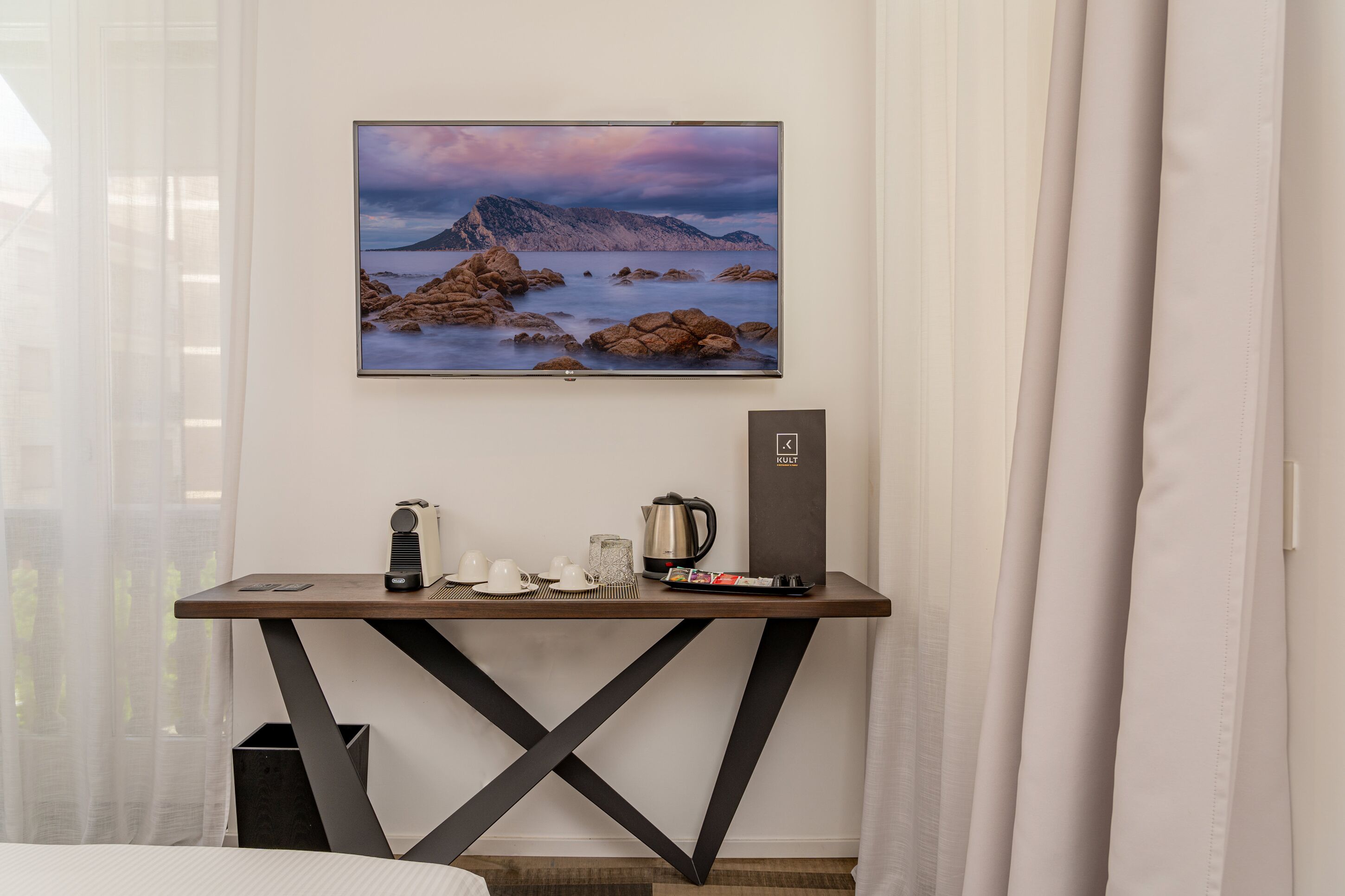 A hotel room with a bed, a desk with a kettle, cups, and a KULT coffee machine.