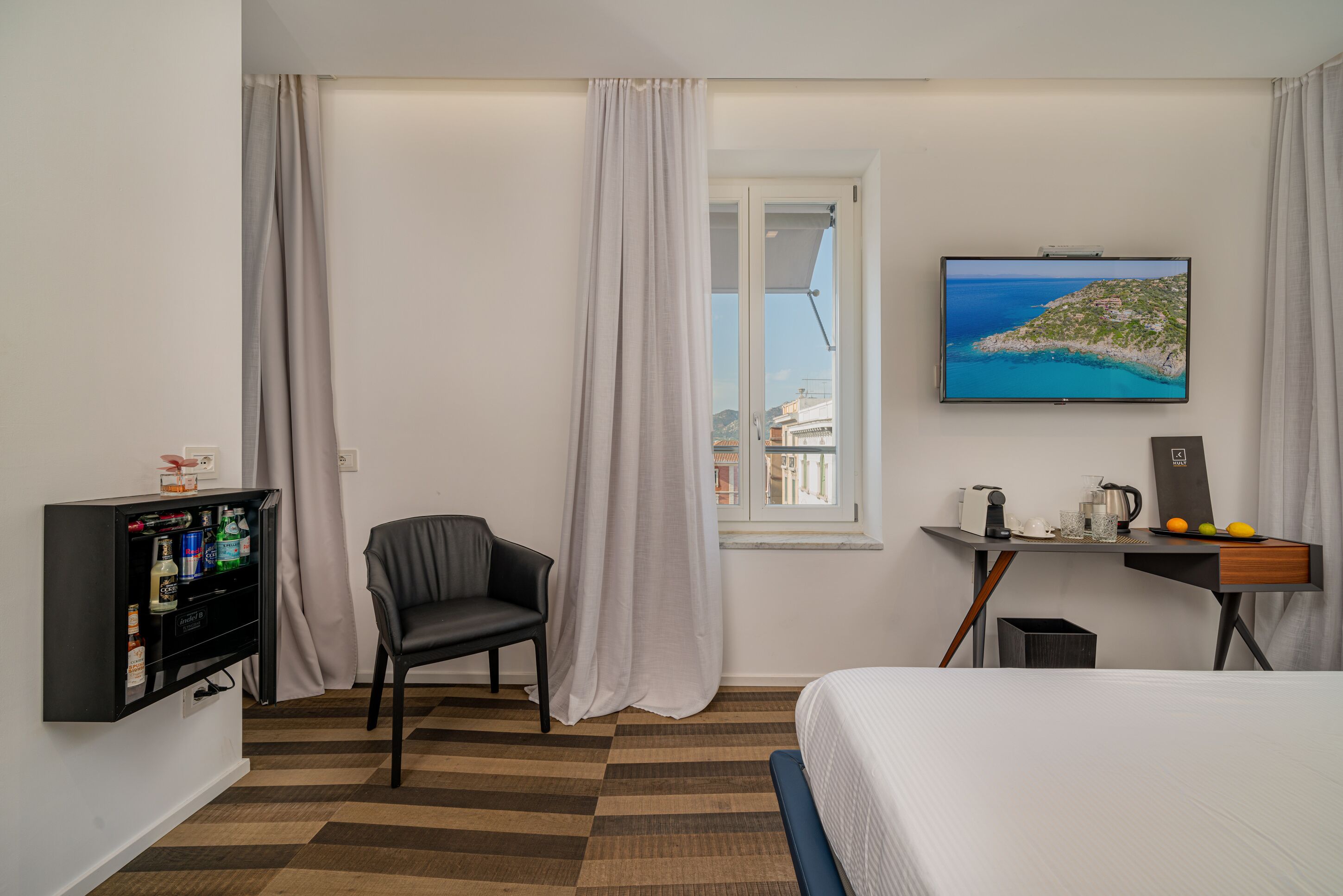 Une chambre d’hôtel équipée d’un lit, d’un bureau avec un ordinateur, d’une chaise, d’un téléviseur fixé au mur et d’une fenêtre donnant sur la mer.