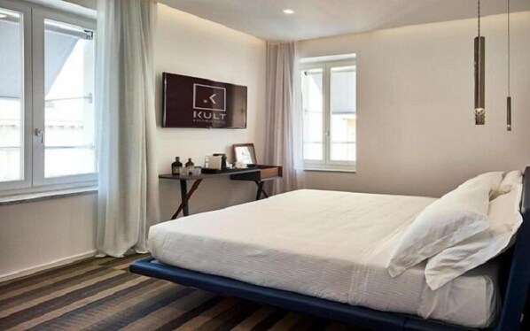 A hotel room with a bed, a desk with a chair, a window, and a wall-mounted sign.