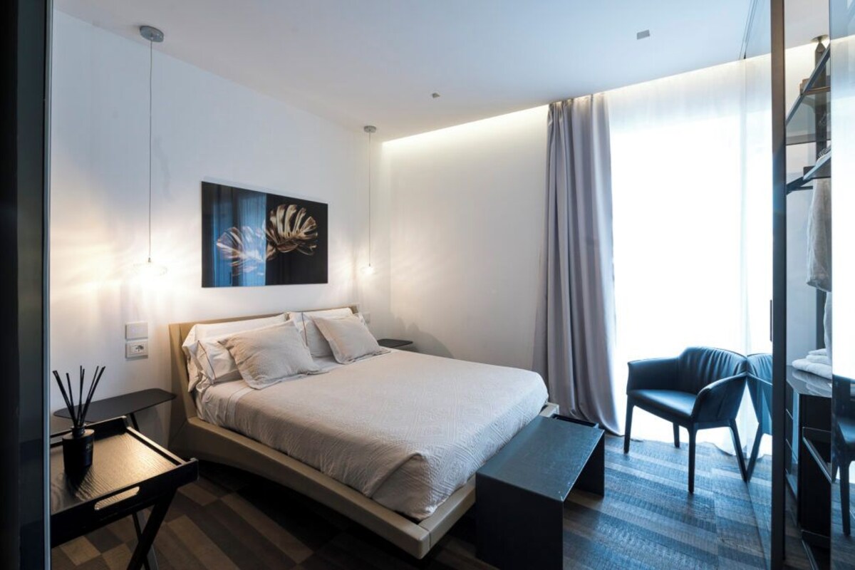 A modern hotel room with a large bed, a desk, a chair, and a painting on the wall.