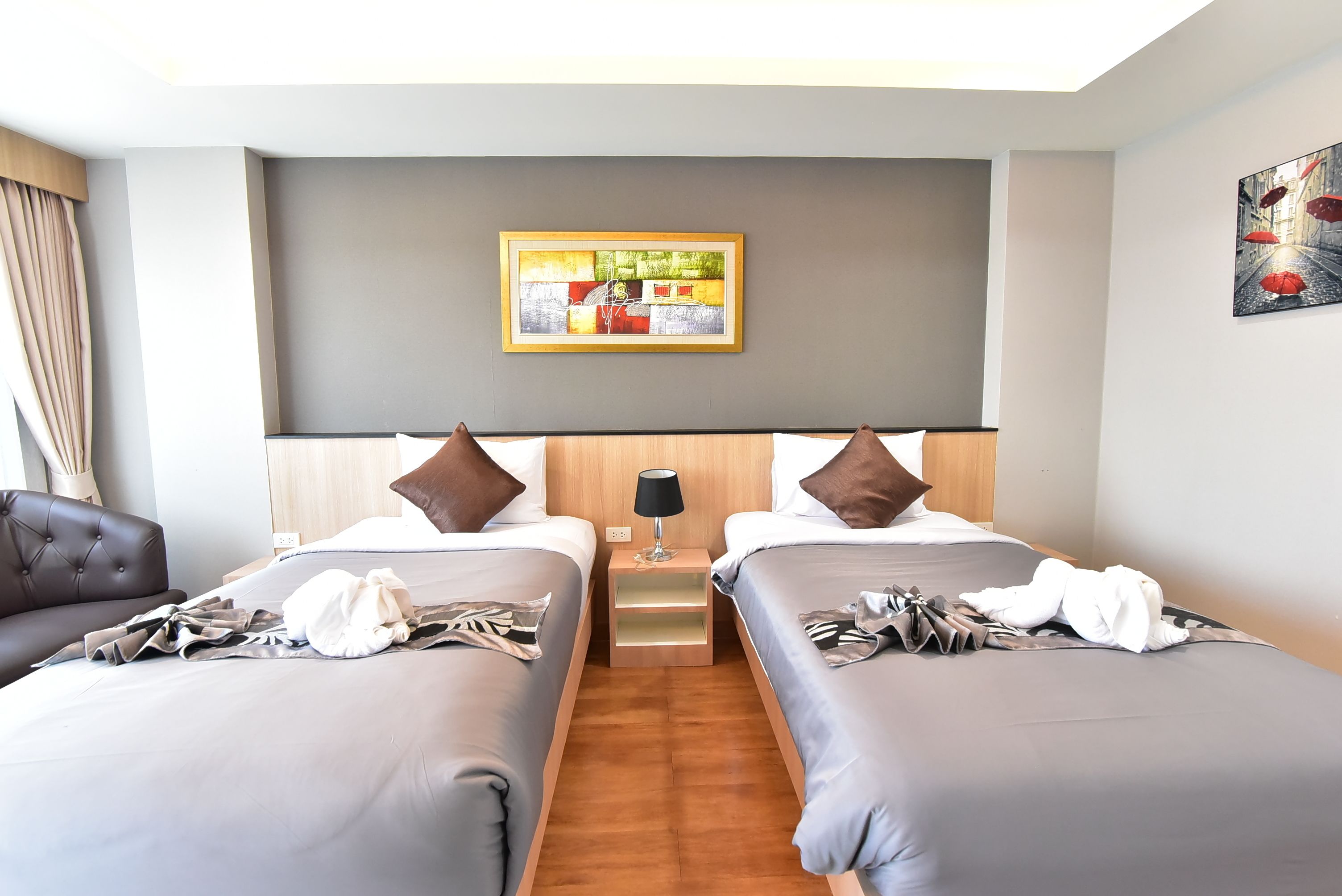 A hotel room with two beds, a nightstand with a lamp, and a painting on the wall.