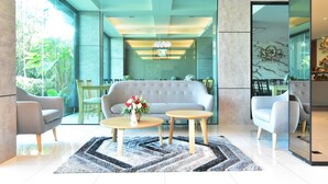 A modern interior with a grey sofa, two round tables, and a decorative vase with flowers. - The U-Time Hotel (Hat Yai)