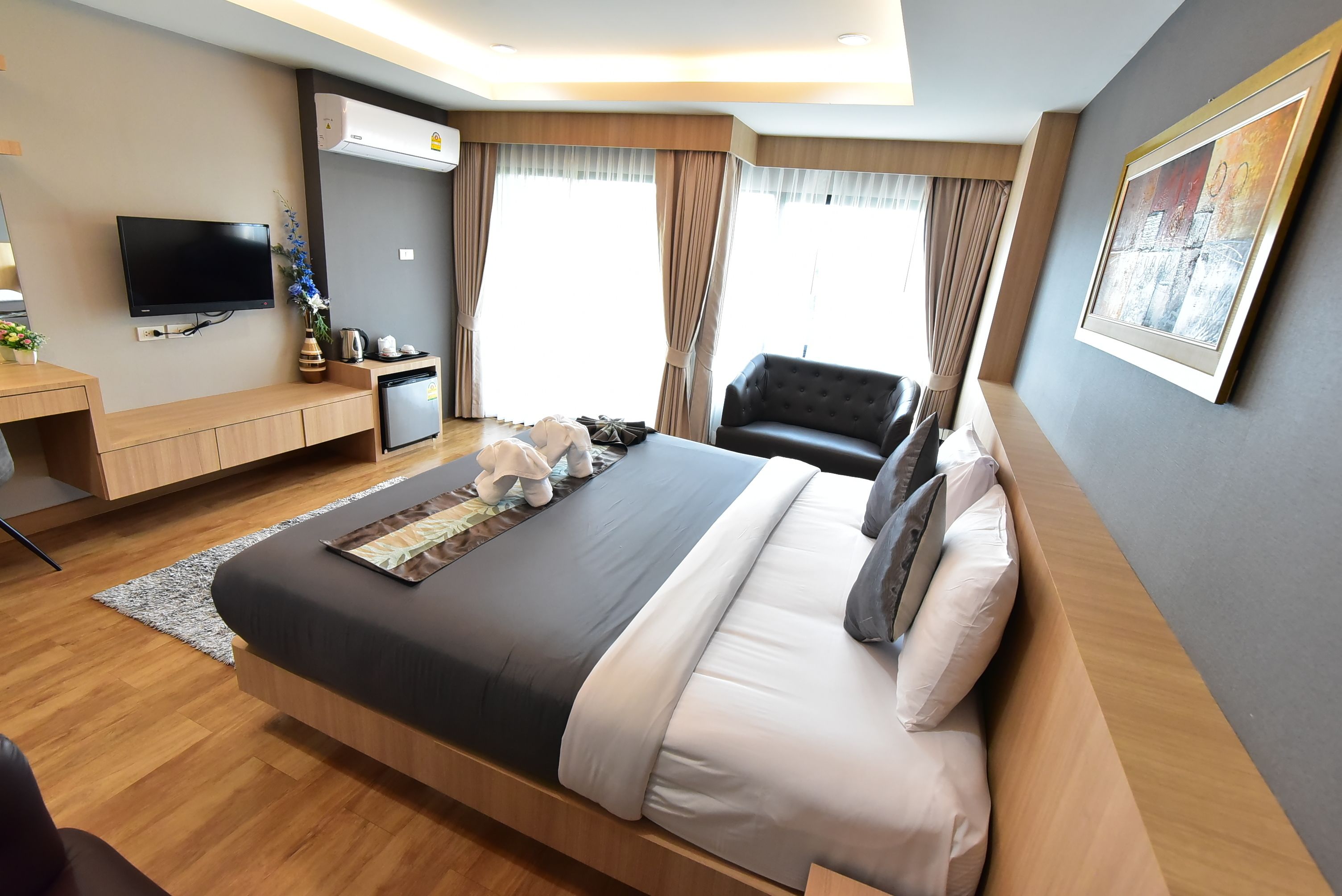A modern hotel room with a large bed, a flat-screen TV, a desk with a coffee machine, and a view of the city through large windows.