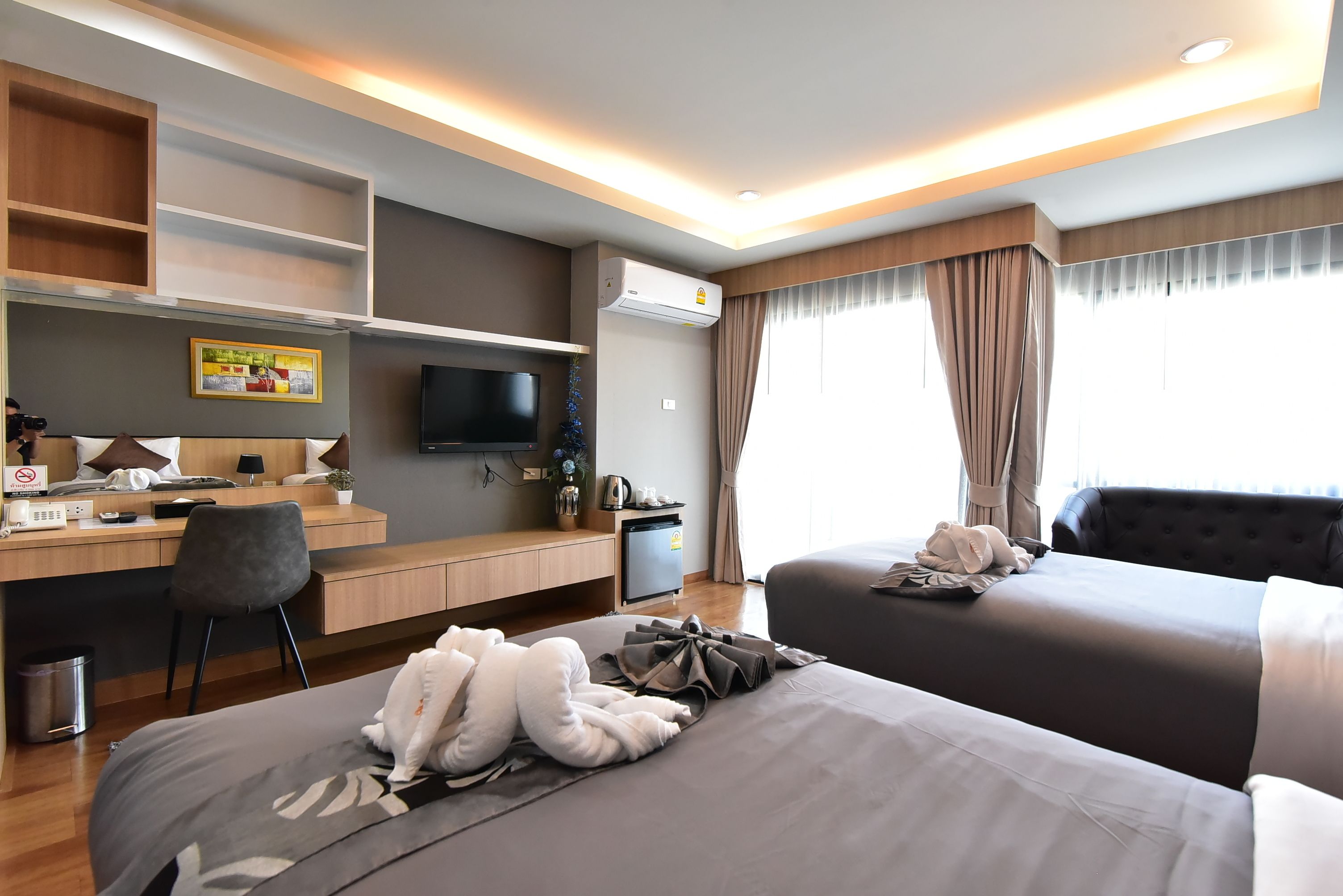 A hotel room with a desk, two beds, a TV, and a window with curtains.