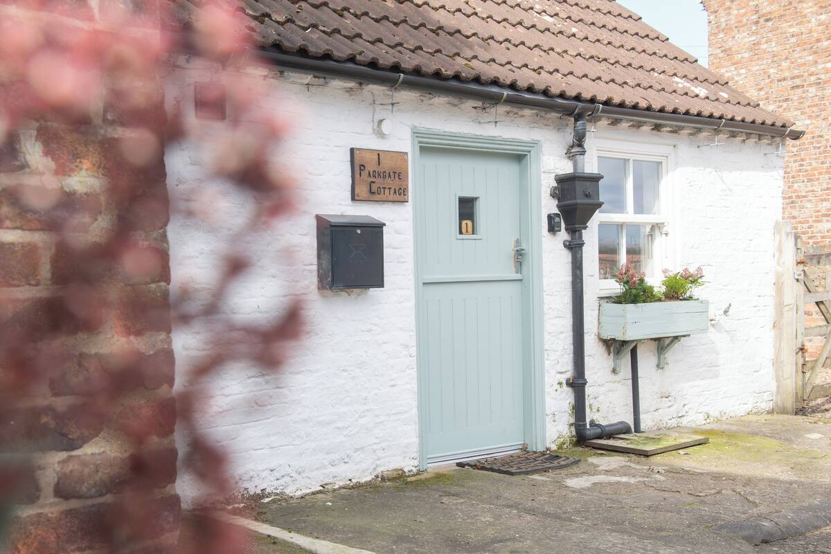 Ein Cottage mit einer hellblauen Tür, einem Schild darüber, einem Briefkasten und einem Blumenkasten.