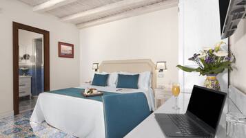 A hotel room with a bed, a laptop on a table, a vase with flowers, and a glass of orange juice.