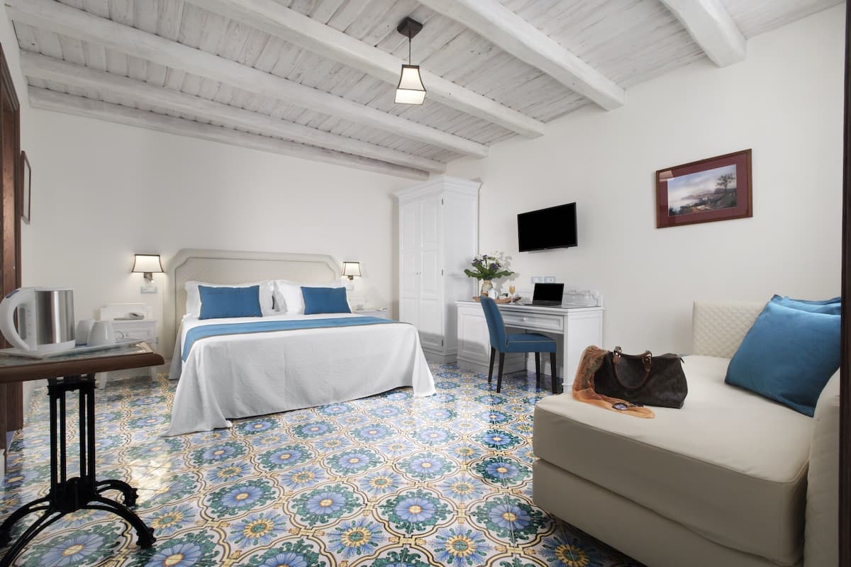 Une chambre d’hôtel équipée d’un lit, d’un bureau, d’une chaise, d’un canapé et d’un téléviseur fixé au mur.
