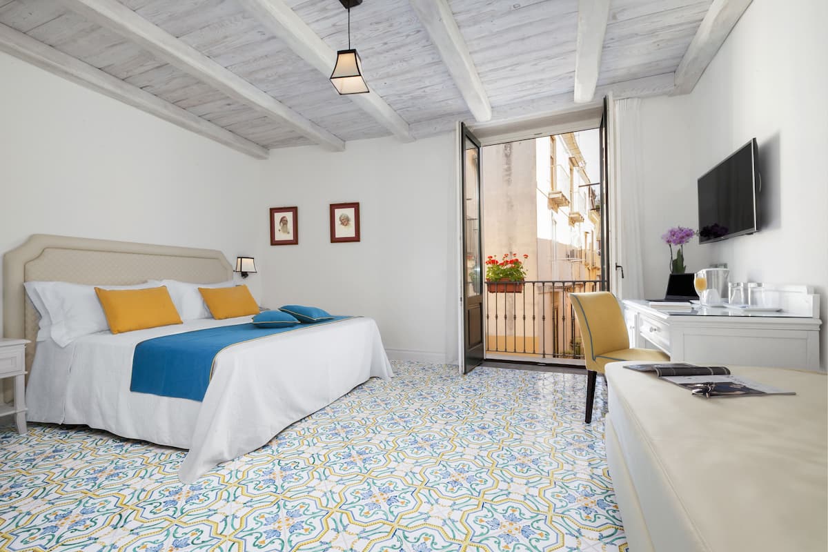 Une chambre à coucher comprenant un lit, un bureau, une chaise, un téléviseur et un balcon agrémenté de plantes.