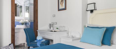 A hotel room with a bed, a desk, a chair, a small table, a mirror, and a picture on the wall.