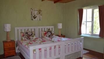 A bedroom with a double bed, two nightstands, a lamp on each nightstand, a window with curtains, and a wall-mounted picture.
