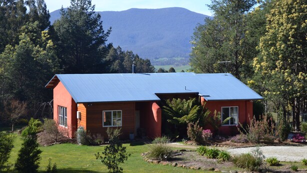 A two-story house with a blue roof, surrounded by a well-maintained garden and trees. - Whispering Spirit Holiday Cottages (Franklin)