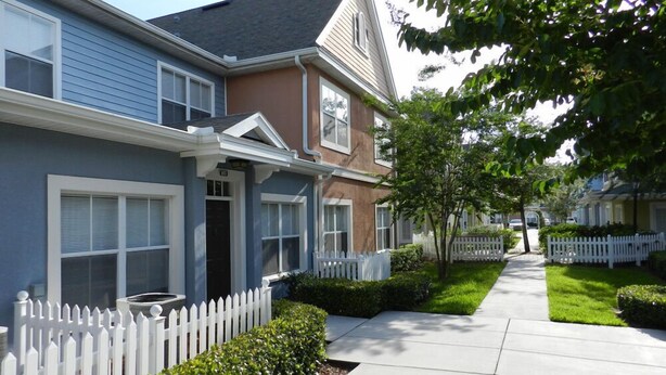 A row of two-story houses with a white picket fence, a sidewalk, and well-maintained lawns.