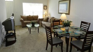 A living room with a sofa, a coffee table, a dining table with chairs, a ceiling fan, and a television.