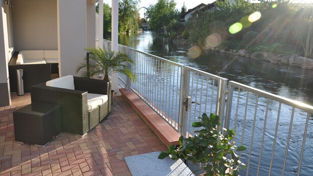 A balcony with wicker furniture and a view of a river. - Gästehaus am Bach - Ferienwohnungen (Rust)
