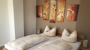 A double bed with a wooden frame, two pillows, and a wall-mounted painting of flowers. - Gästehaus am Bach - Ferienwohnungen (Rust)