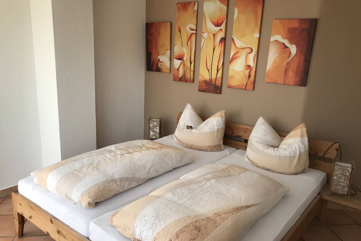 A double bed with a wooden frame, two pillows, and a wall-mounted painting of flowers.