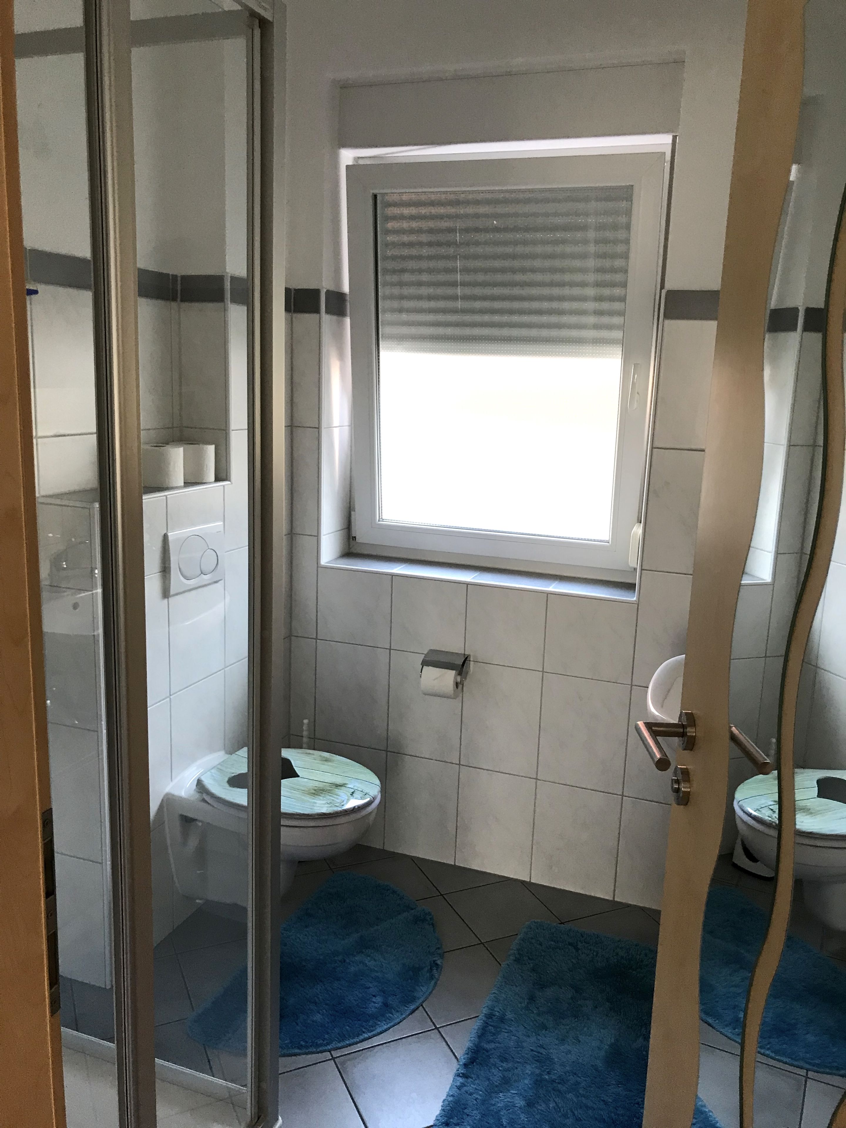 Ein Badezimmer mit Toilette, Bidet, Duschkabine aus Glas und einem Fenster mit Jalousien.