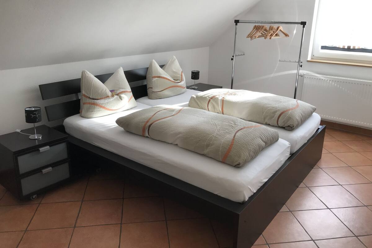 A bedroom with a bed, two bedside tables, a nightstand, a window with a view, and a radiator.