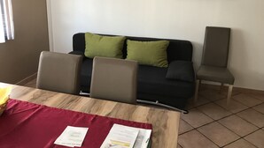 A room with a wooden table, two green cushions on a black sofa, and a painting on the wall. - Gästehaus am Bach - Ferienwohnungen (Rust)