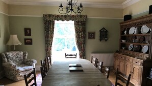 A dining room with a wooden table, chairs, a floral armchair, a chandelier, and a cabinet with dishes. - Byrness House (Newcastle-upon-Tyne)