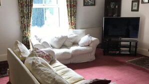 A living room with a beige sofa, a television on a stand, and floral curtains. - Byrness House (Newcastle-upon-Tyne)