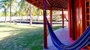 Un espace extérieur abrité, doté d’un hamac, de palmiers et d’un bâtiment avec un toit rouge.