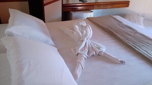 Un lit bien fait, agrémenté d’une sculpture en serviette, de coussins blancs et d’une couverture.