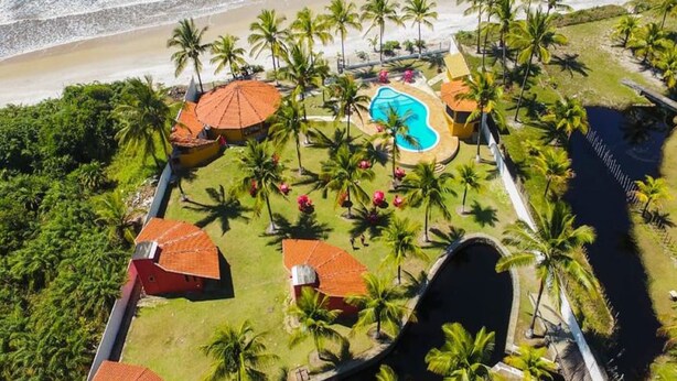Vue aérienne d’un complexe hôtelier doté d’une piscine, de palmiers et d’un accès direct à la plage.