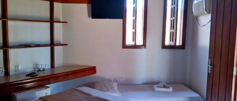 A bedroom with two beds, a wooden shelf unit, a flat-screen TV, and an air conditioning unit.