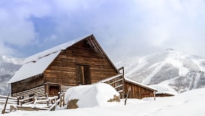 A wooden cabin with a snow-covered roof and a wooden fence in a snowy mountainous area. - Lodge E 103 (Steamboat Springs)