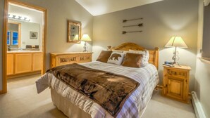 A bedroom with a large bed, wooden nightstands, a mirror, and wall-mounted arrows. - Quail Run 3393 (Steamboat Springs)