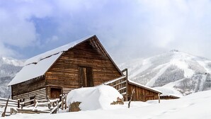 A wooden cabin with a snow-covered roof and a wooden fence in a snowy mountainous area. - Mustang Run 4A (Steamboat Springs)
