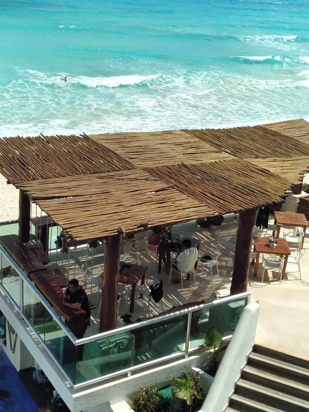 Un restaurante frente al mar con una pérgola de madera, mesas al aire libre y vistas al océano.