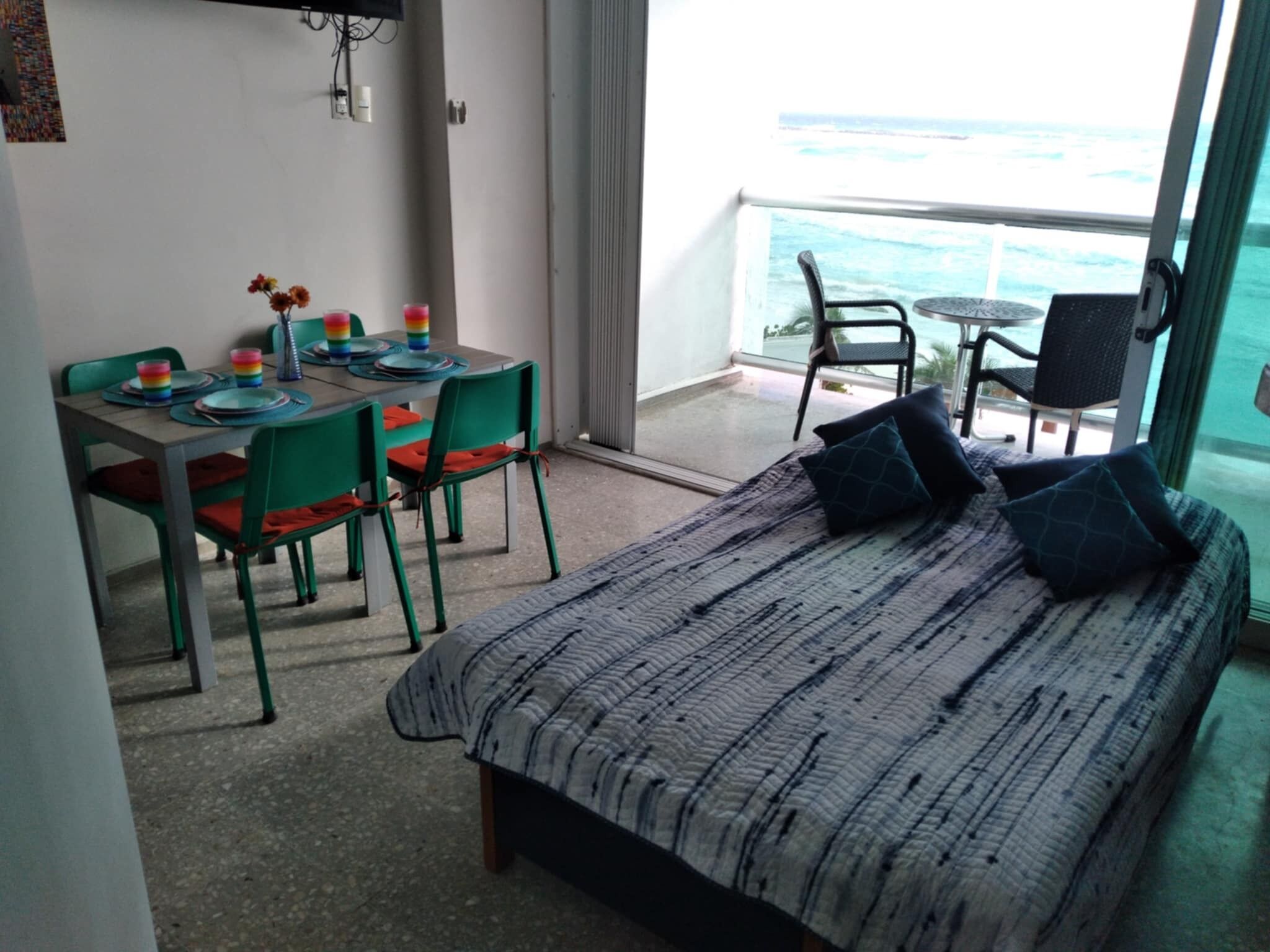 A room with a bed, a dining table with chairs, and a view of the ocean.