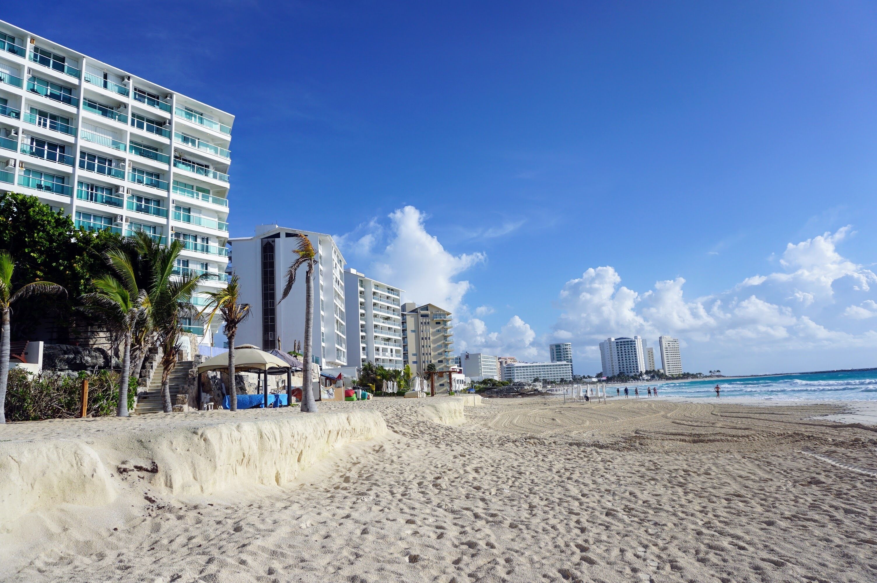 A beach with a high-rise hotel, palm trees, and a clear blue sky.