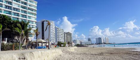 A beach with a high-rise hotel, palm trees, and a clear blue sky.