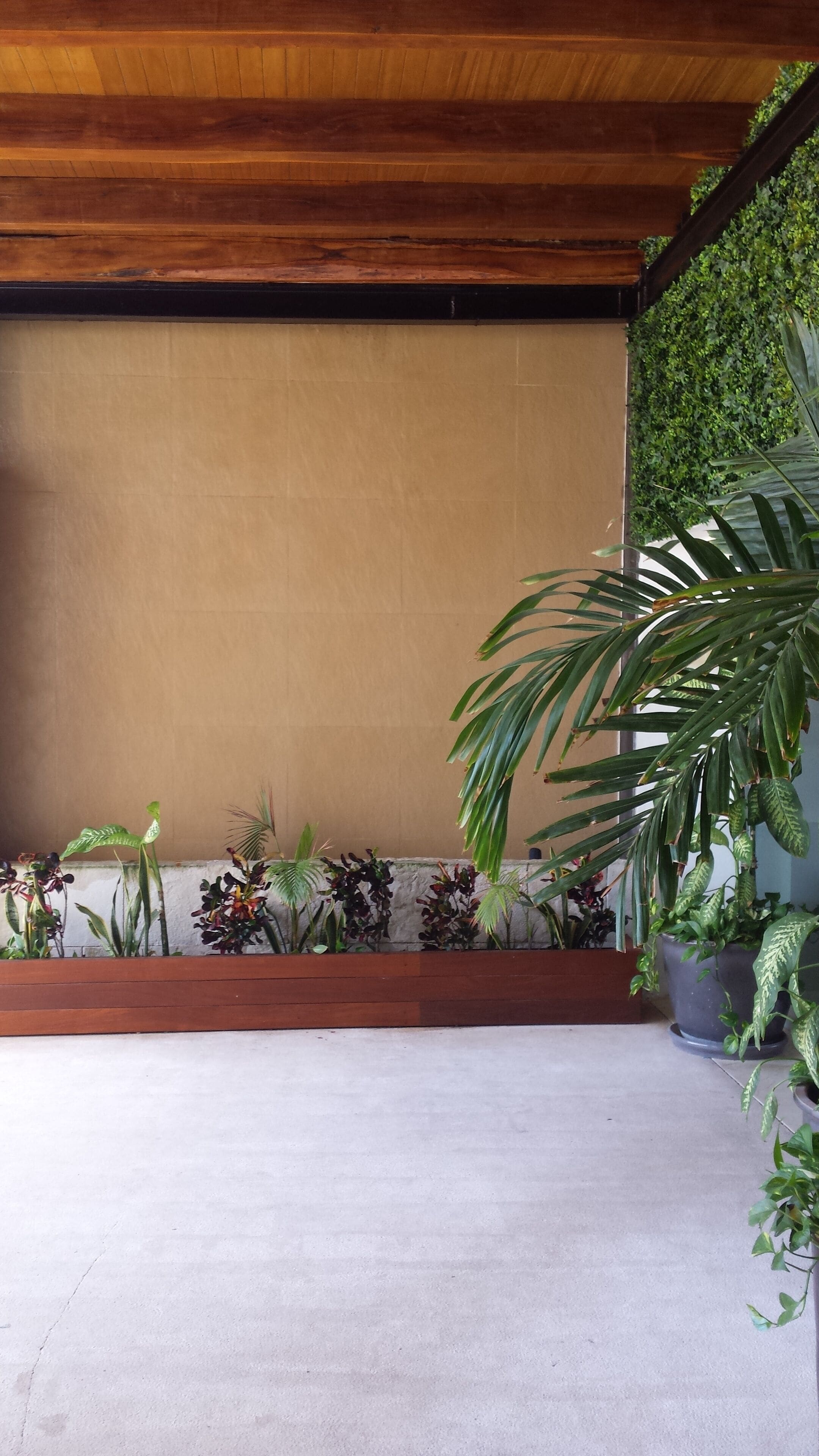 A covered patio area with a concrete floor, wooden ceiling beams, and various potted plants.