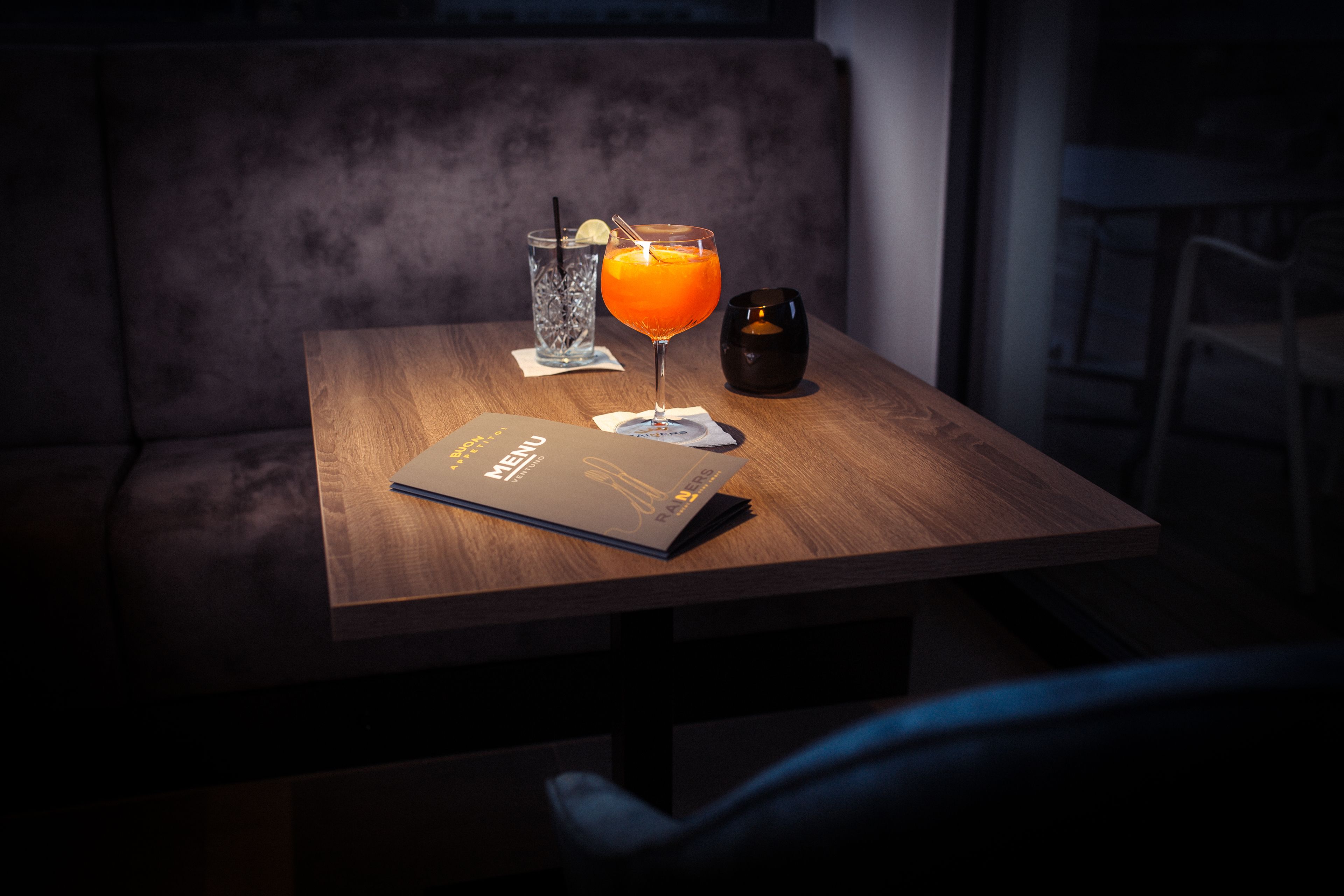 A wooden table with a menu, a glass of orange juice, and a glass of water.