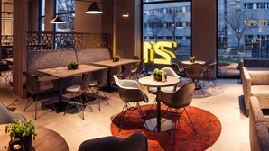 Een modern interieur met diverse zitplaatsen, zoals tafels, stoelen en banken. Er staan potplanten op tafels en een groot raam biedt uitzicht op de stad.