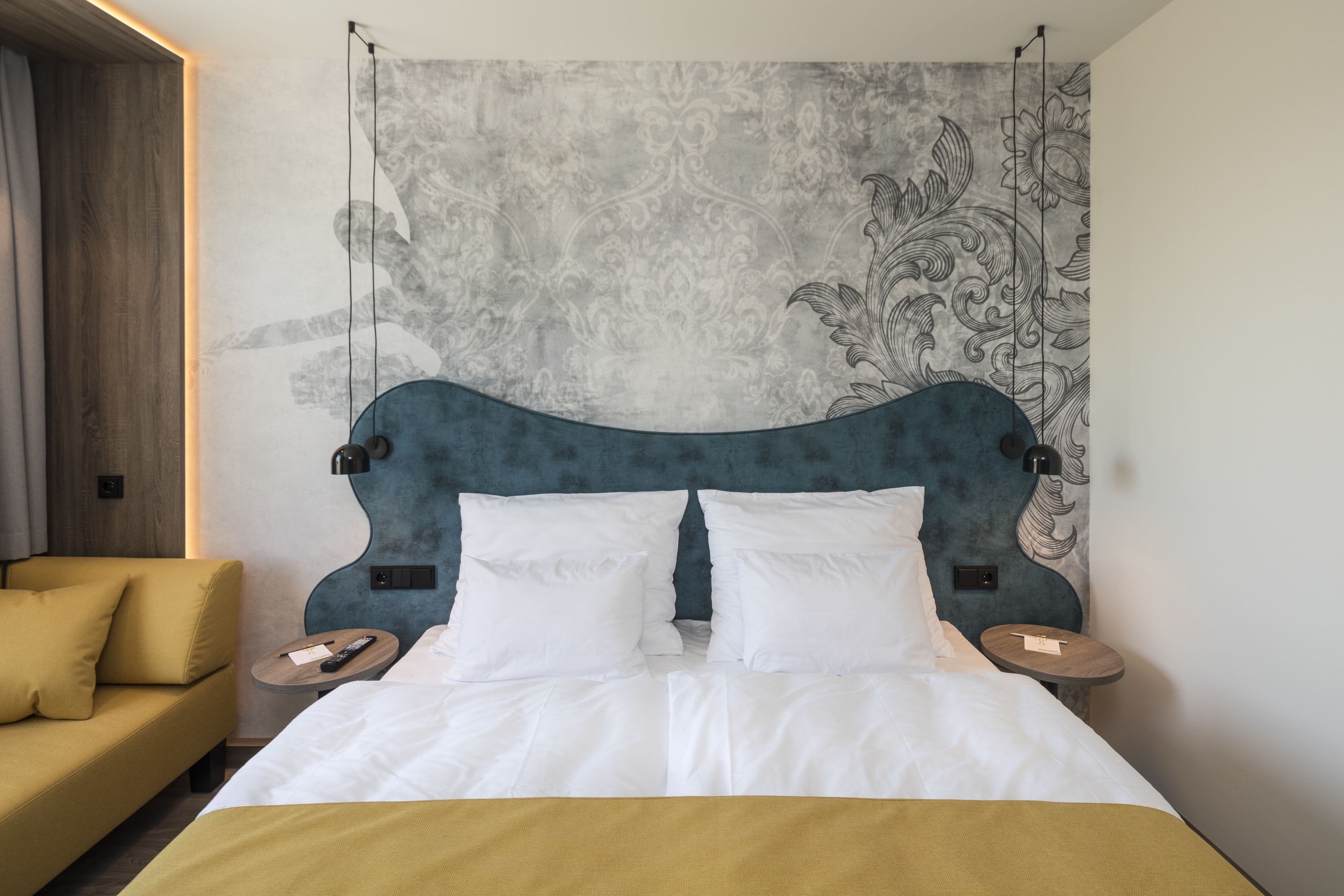 A neatly made bed with white linens, a blue upholstered headboard, and two bedside tables with lamps.