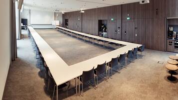 Konferenssihuone, jossa on pitkä pöytä, tuoleja, projektori ja valkokangas.