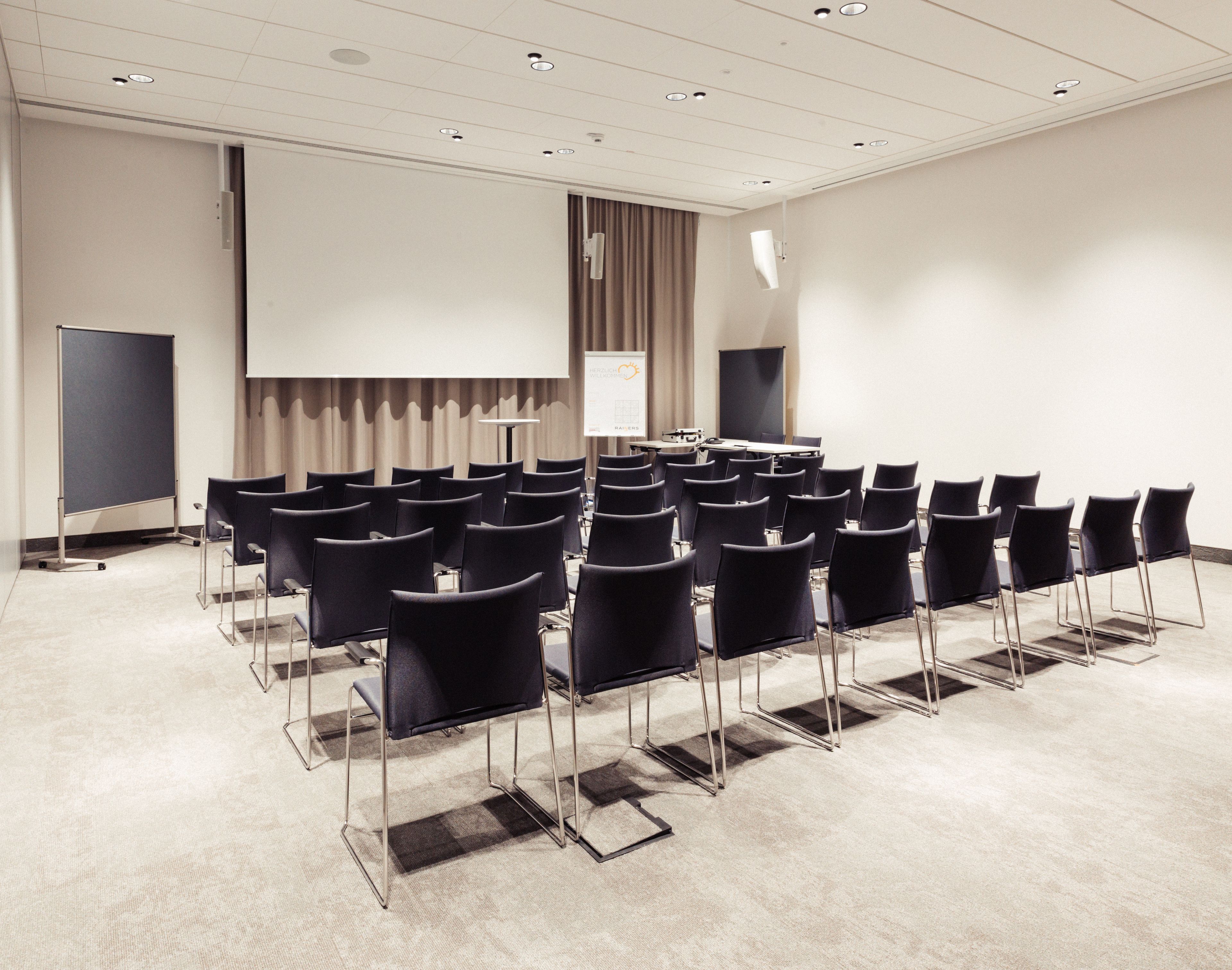 A conference room with rows of chairs, a projector screen, and a presentation screen.