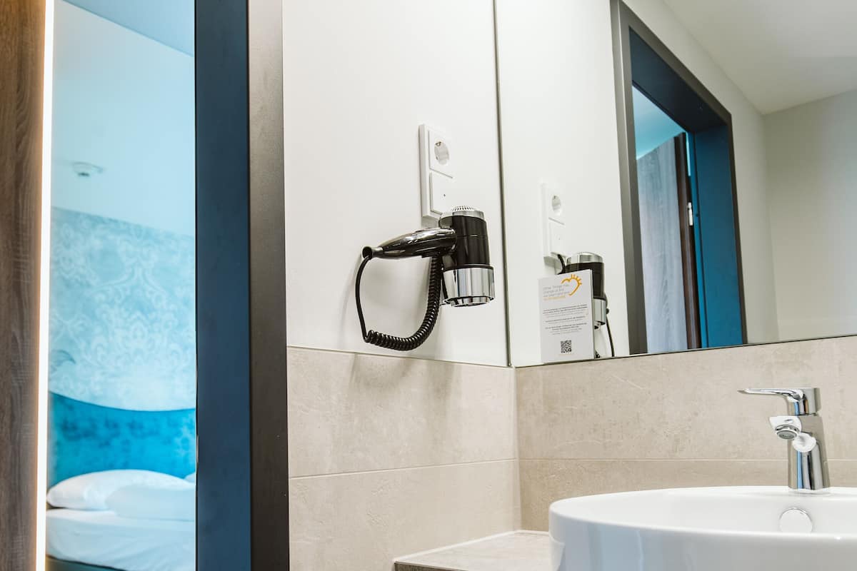 A modern bathroom with a large mirror, a sink, and a hairdryer on the wall.