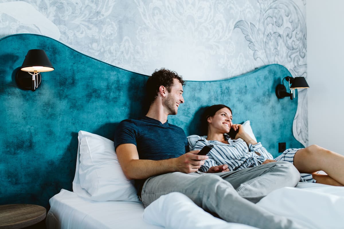A bedroom with a teal headboard, two bedside lamps, and a patterned wall.
