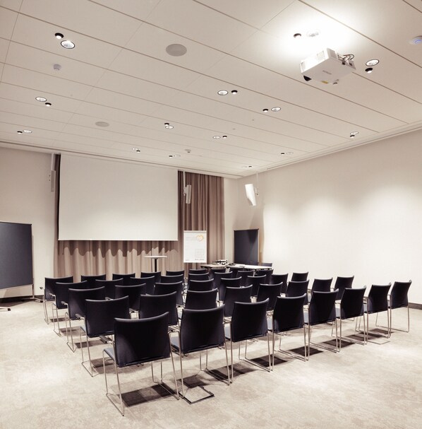 A conference room with rows of chairs, a projector screen, and a presentation screen.
