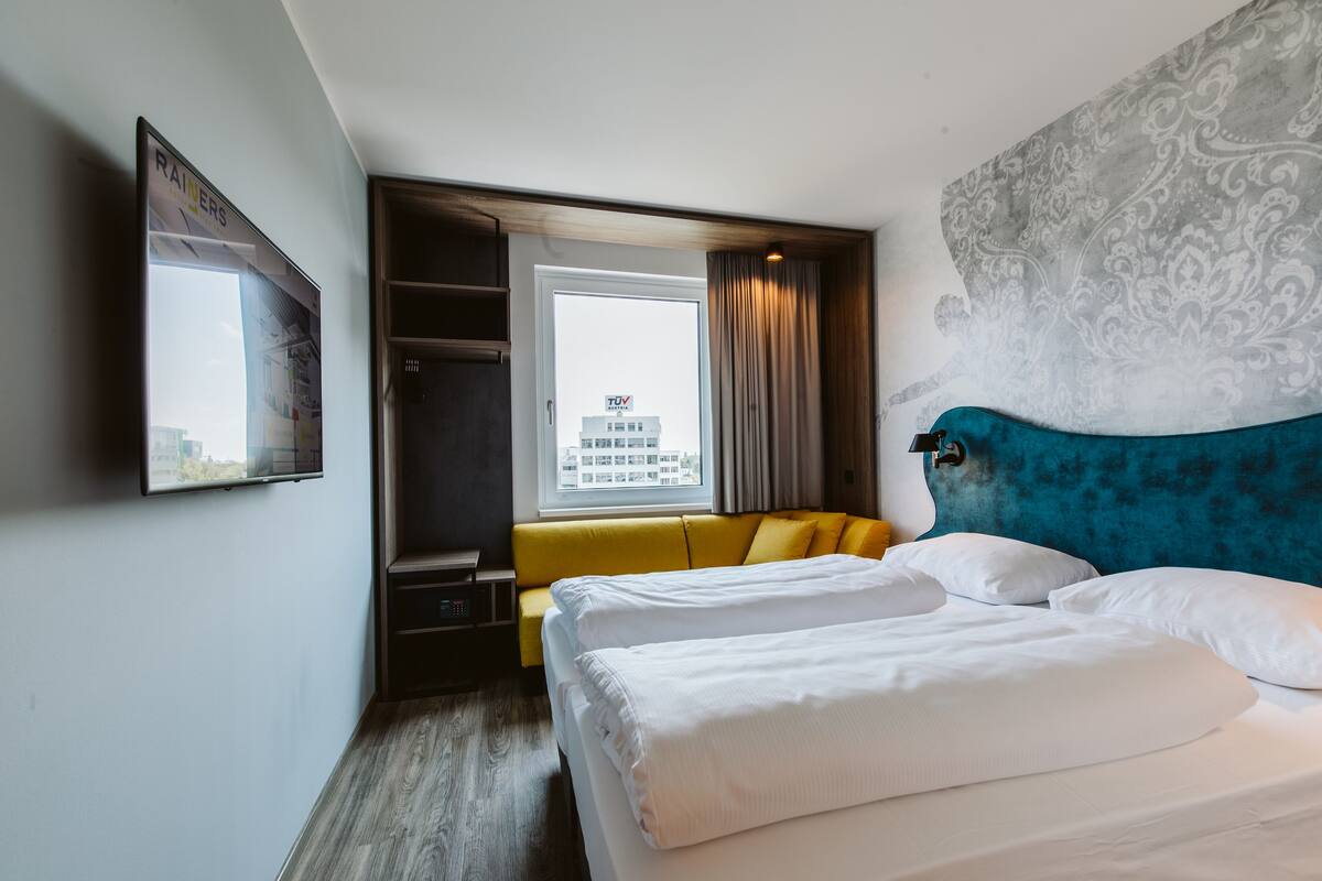 A hotel room with a bed, a sofa, a TV, and a window with curtains.