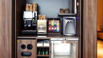 A compact kitchenette with a coffee machine, toaster, mini-fridge, and shelves with cups and glasses.