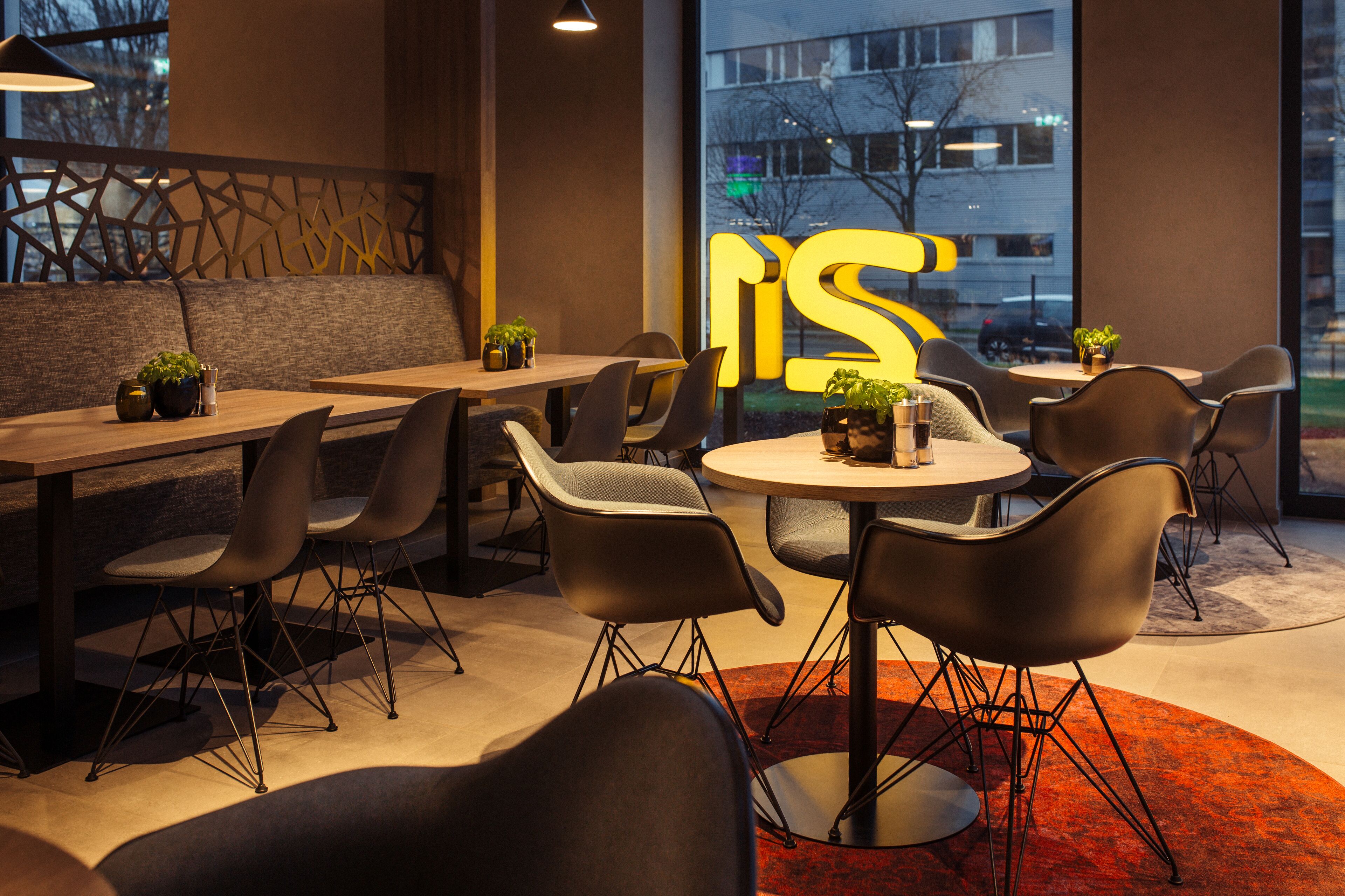 A modern dining area with a mix of round and rectangular tables, black chairs, and potted plants.